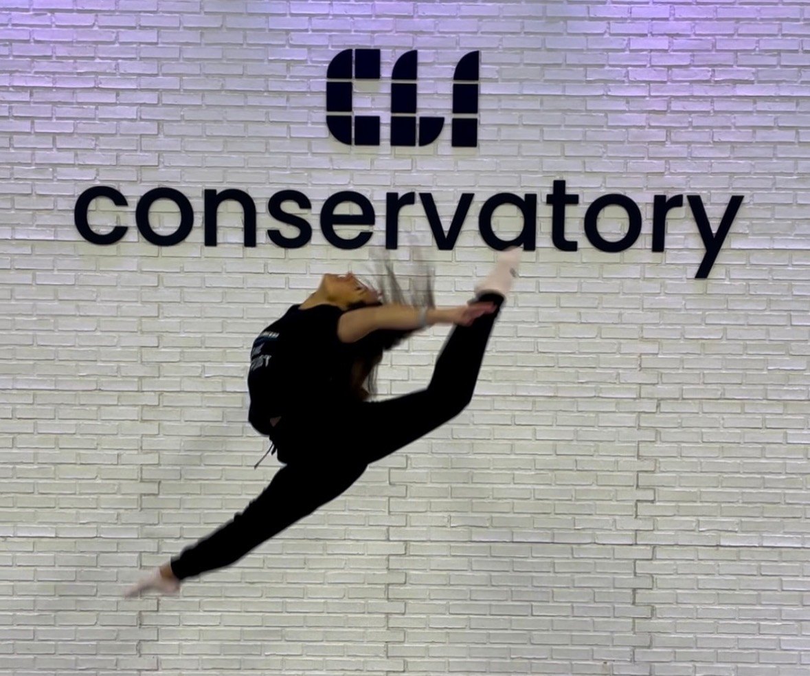 DFD Dance Specialist Dr. Audrey Lugo leaping in front of the CLI Conservatory sign